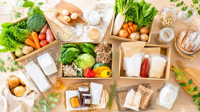無添加宅配サービスで届く野菜・パン・調味料・卵・豆腐を木のテーブルに並べた俯瞰写真