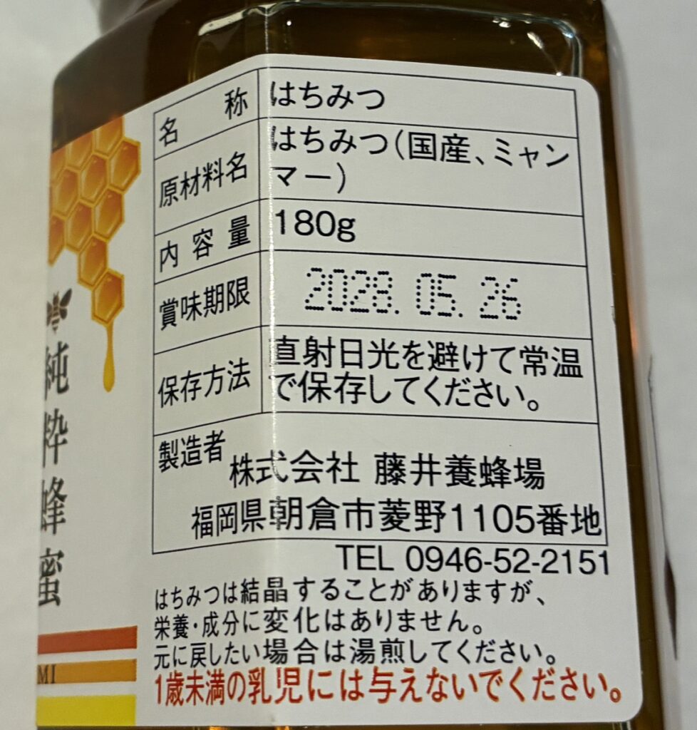 みつばちの恵の裏面ラベル。原材料名は「はちみつ(国産、ミャンマー)」、内容量180g、製造者は福岡県朝倉市の藤井養蜂場と表示されている
