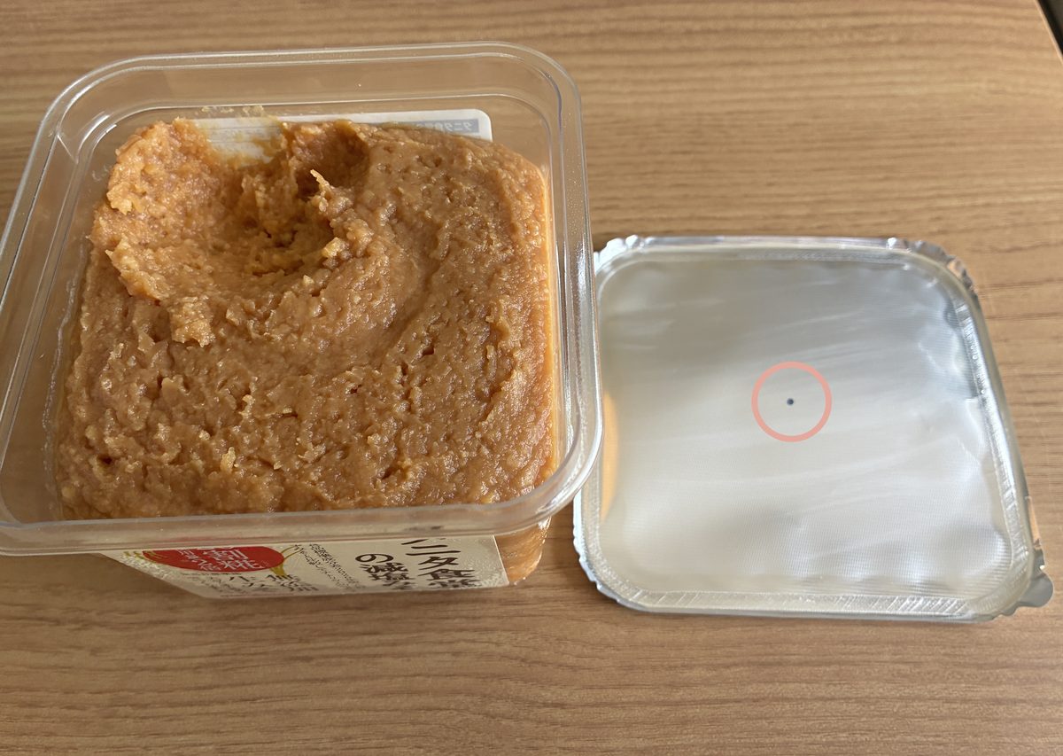 タニタ食堂の減塩みそのカップと、外した蓋のフィルム。フィルムの真ん中の黒い点(空気の穴)をピンクの丸で囲んでいる